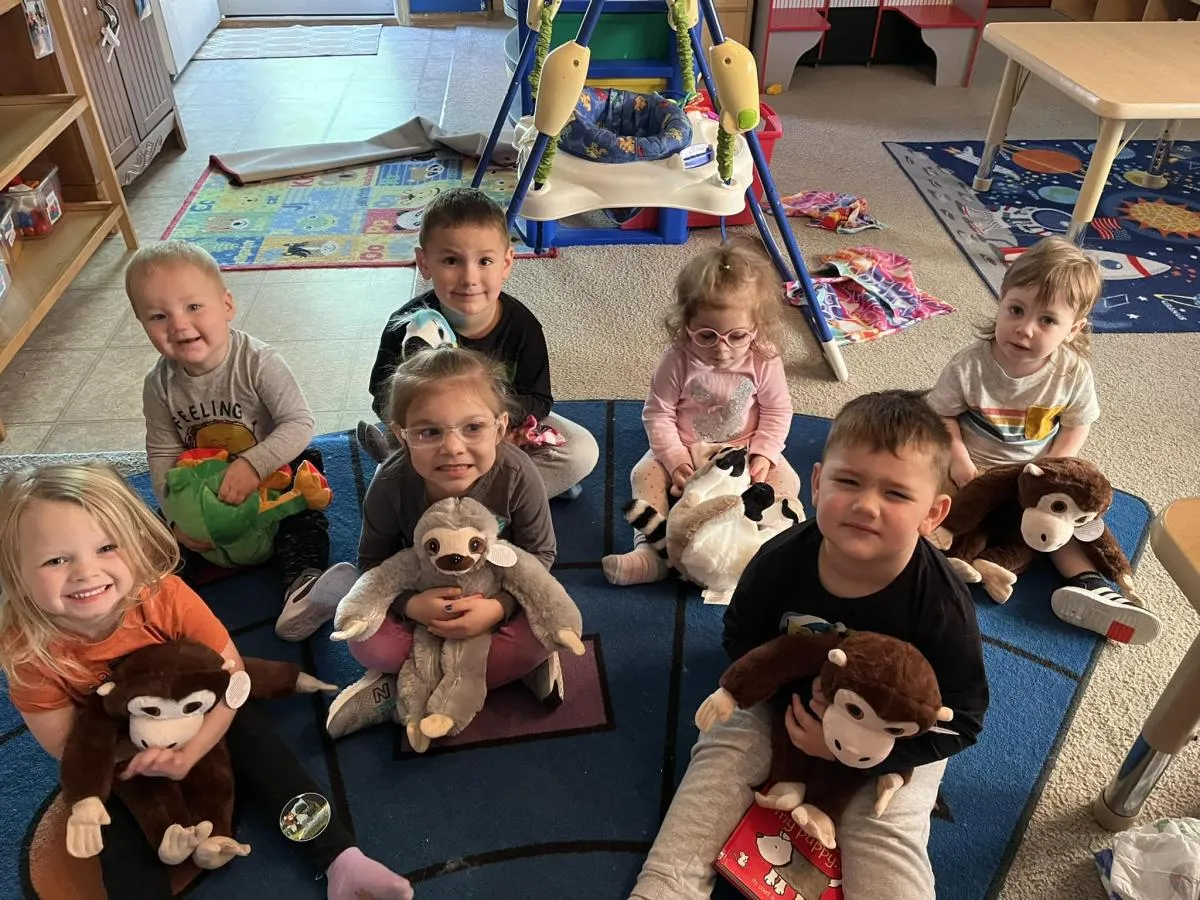 Group of kids gathered on floor, surrounded by plush toys, enjoying playtime.